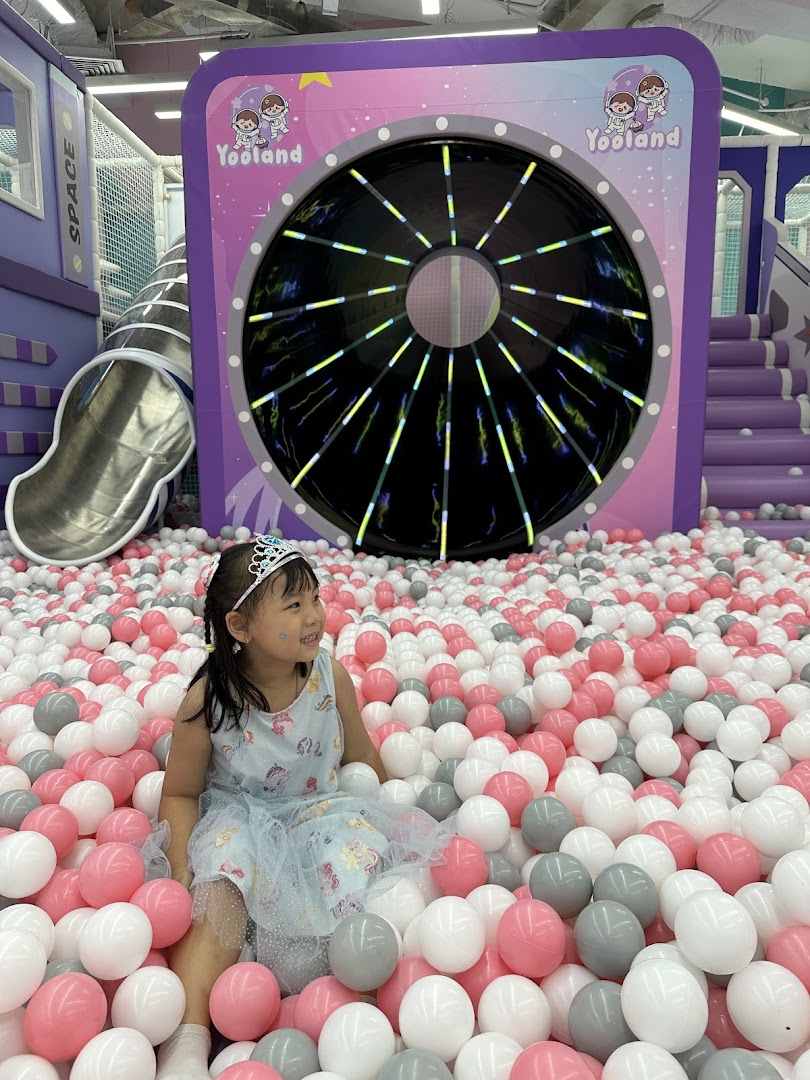 A happy child plays in a vibrant ball pit at Yooland, an exciting indoor playground with space-themed elements.