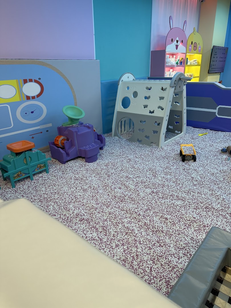 A vibrant indoor play area featuring a large pit filled with small particles and various colorful play structures.