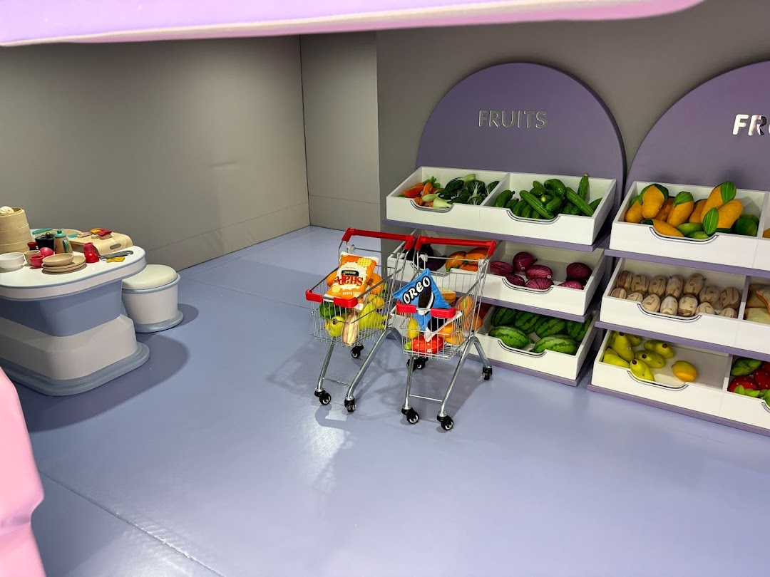 A vibrant play area at Yooland featuring a miniature supermarket with toy fruits, vegetables, and shopping carts.