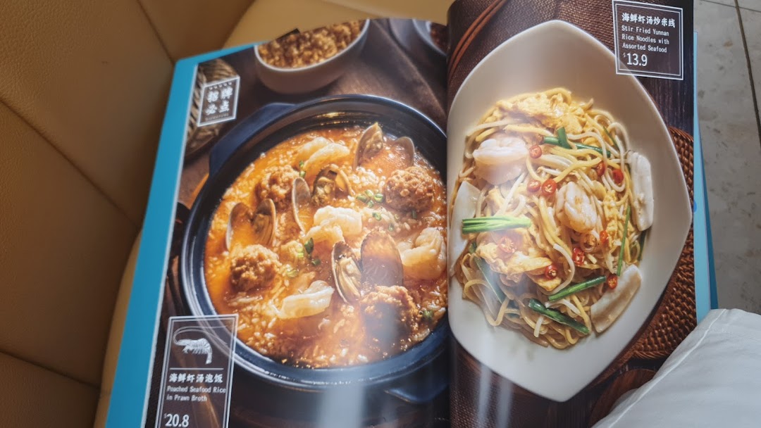 An open menu displaying two seafood dishes: Poached Seafood Rice and Stir Fried Yunnan Rice Noodles.