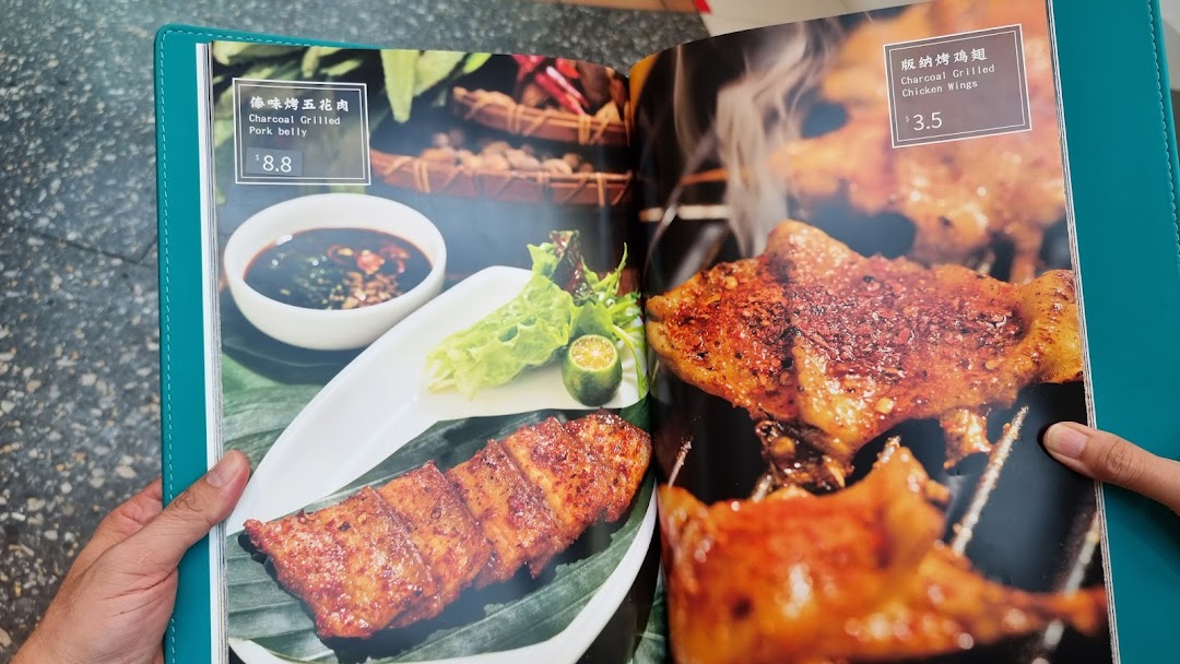 A close-up of a menu displaying charcoal-grilled pork belly and chicken wings with prices.