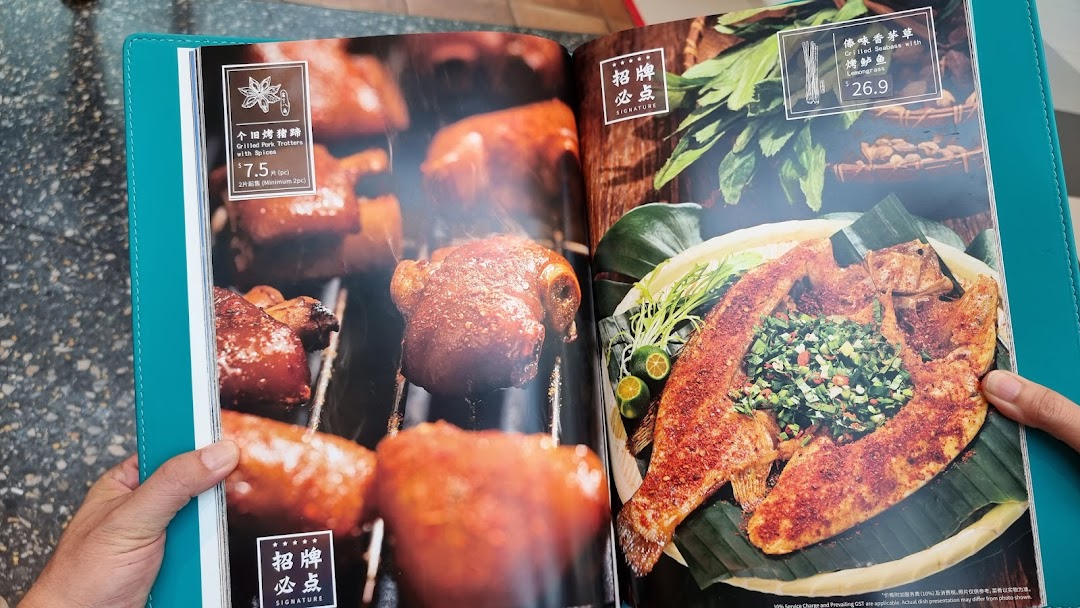 A person holds an open menu displaying YUN NANS' signature grilled pork trotters and grilled seabass.